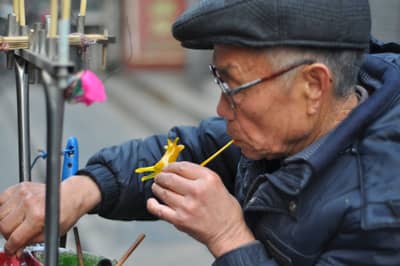 A sugar artisan blowing air through a straw to inflate a hot sugar figure