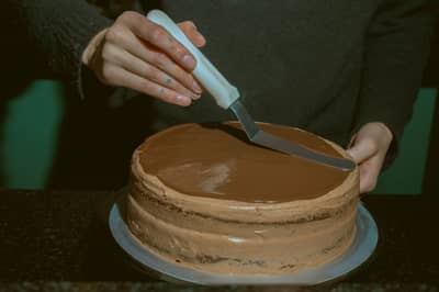 A thin crumb coat being smoothed over a layer cake with a spatula