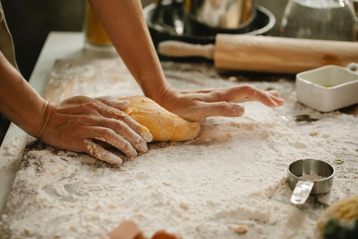 Hands kneading bread dough on a floured counter