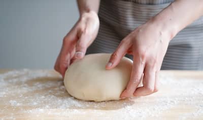 A finger gently pressing a proofed ball of dough