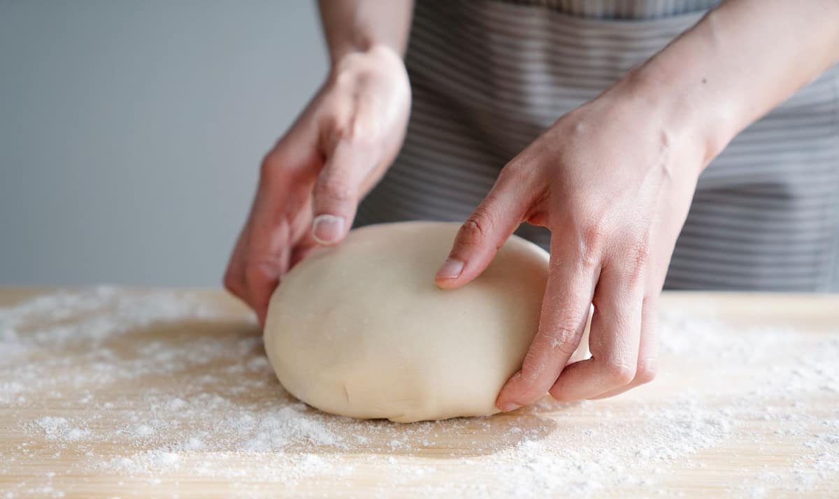 A finger gently pressing a proofed ball of dough