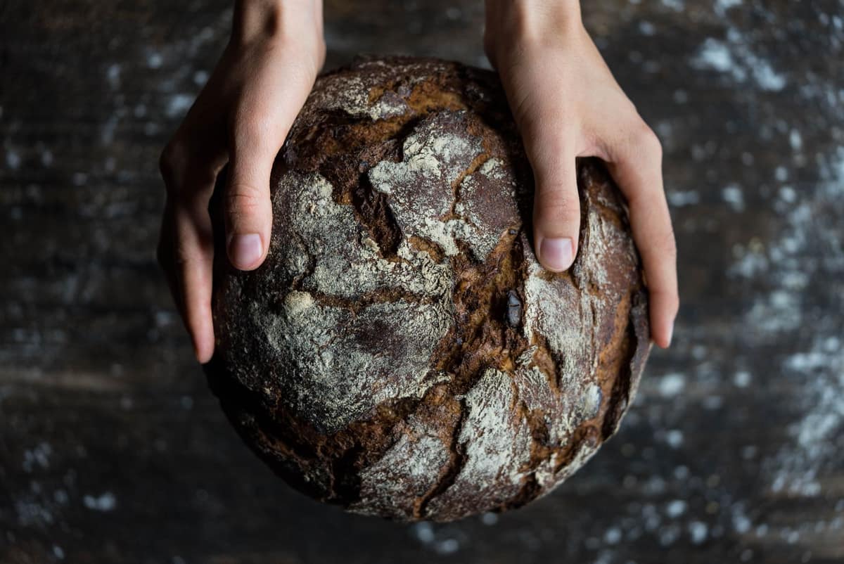 Hands holding a rustic loaf baked with reclaimed grains